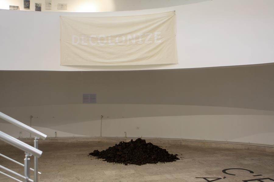 earth on the floor and a banner with text decolonixe on the wall