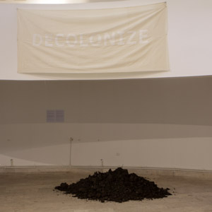 earth on the floor and a banner with text decolonixe on the wall